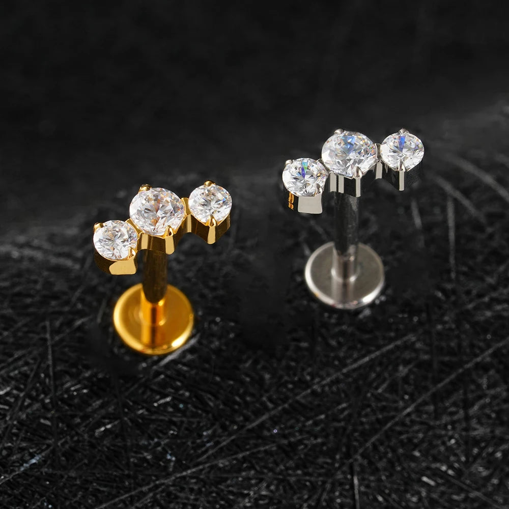 Pair of gold and silver earrings with clear gemstones on a textured black surface.